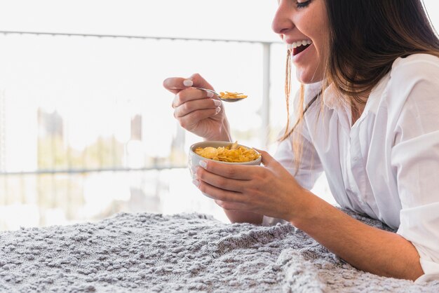 Lächelnde junge Frau, welche die Corn-Flakes mit Löffel isst