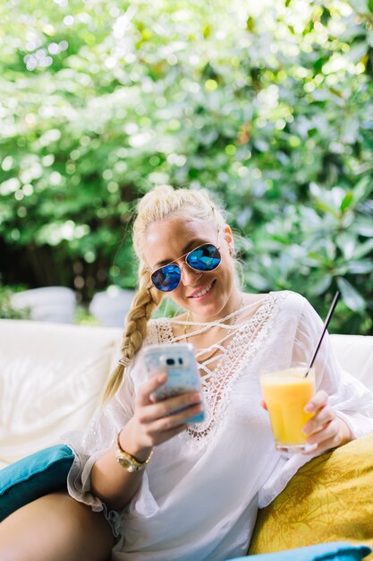 Lächelnde junge Frau, welche die moderne Sonnenbrille hält Glas Saft trägt