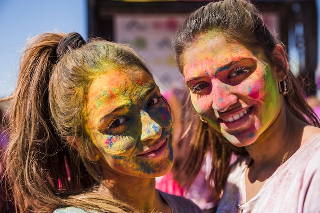 Lächelnde junge Frauen mit holi Farbe auf ihrem Gesicht, das Kamera betrachtet