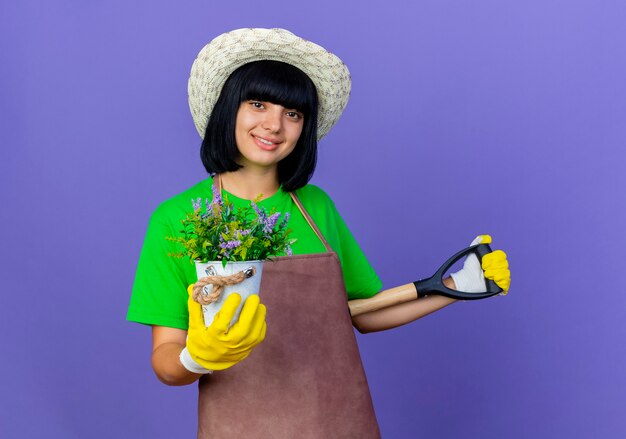 Lächelnde junge Gärtnerin in Uniform mit Gartenhut und Handschuhen