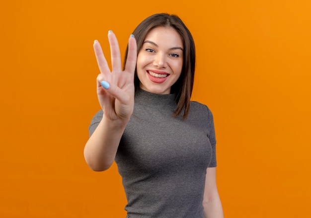 Lächelnde junge hübsche Frau, die drei mit Hand lokalisiert auf orange Hintergrund mit Kopienraum zeigt