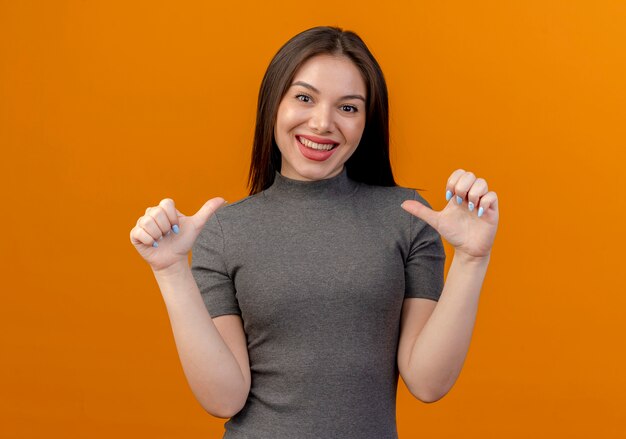 Lächelnde junge hübsche Frau, die lokalisiert auf orange Hintergrund zeigt