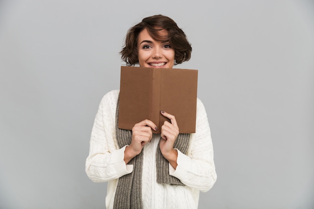 Lächelnde junge hübsche Frau, die Schal liest Buch trägt.