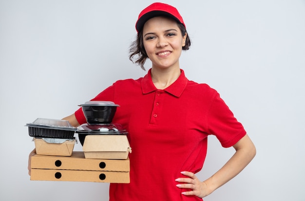 Lächelnde junge hübsche Lieferfrau, die Lebensmittelbehälter und Verpackungen auf Pizzakartons hält