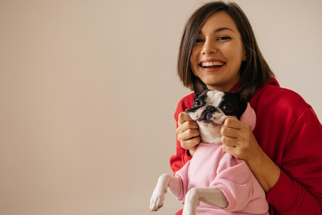 Lächelnde junge kaukasische Frau, die ihre pet39s-Wangen im Hoodie auf weißem Hintergrund hält Liebe zwischen Hund und Besitzer Konzept