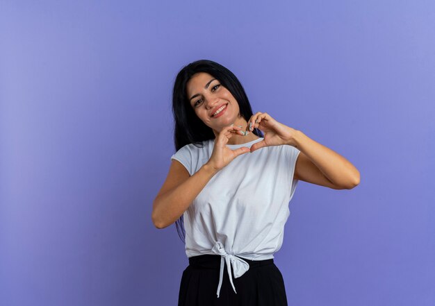 Lächelnde junge kaukasische Frau gestikuliert Herzhandzeichen