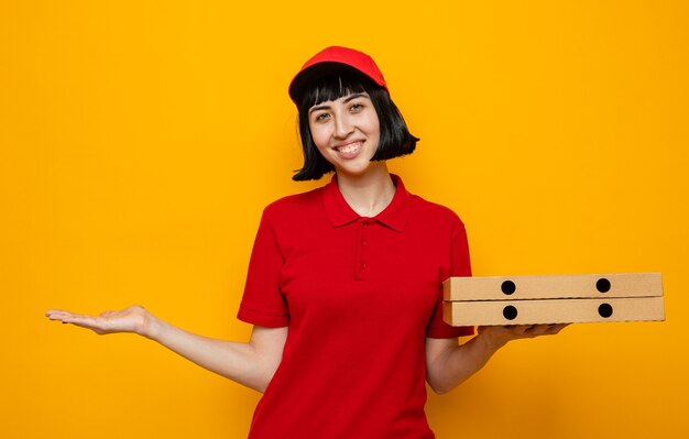 Lächelnde junge kaukasische Lieferfrau, die Pizzakartons hält und ihre Hand offen hält