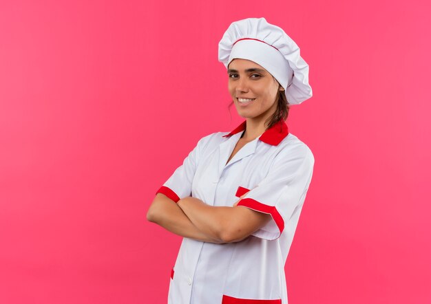 Lächelnde junge Köchin, die Kochuniform trägt, die Hände mit Kopienraum kreuzt