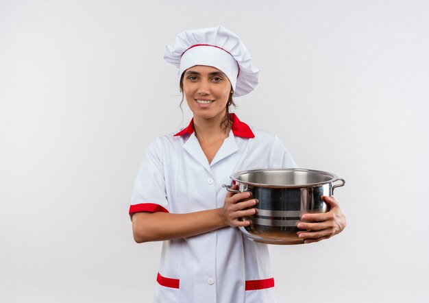 Lächelnde junge Köchin, die Kochuniform trägt, die Topf mit Kopienraum hält