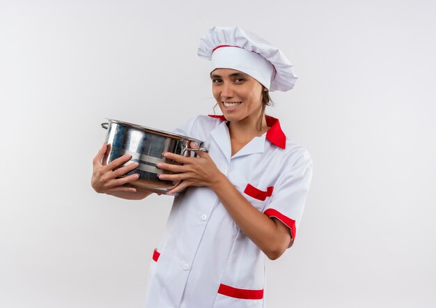 Lächelnde junge Köchin, die Kochuniform trägt, die Topf mit Kopienraum hält
