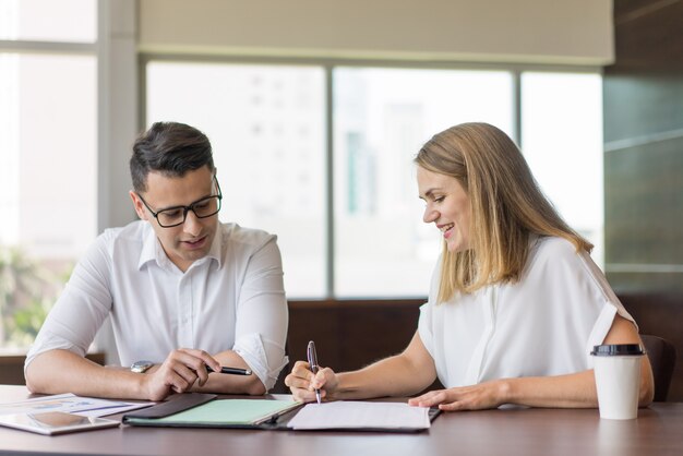 Lächelnde junge Kollegen, die mit Dokumenten im Büro arbeiten.