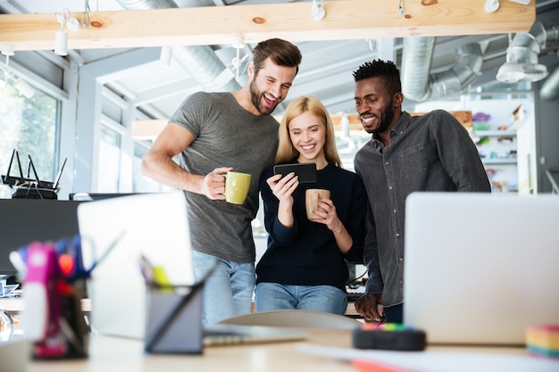 Ein Foto eines Teams, das in einem hell beleuchteten Büro steht und lacht, symbolisiert eine positive Kommunikationskultur am Arbeitsplatz. 