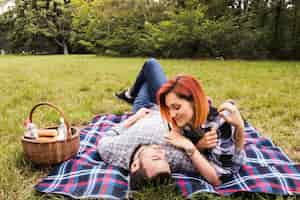 Kostenloses Foto lächelnde junge paare, die auf decke über grünem gras am picknick liegen