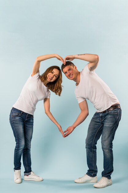 Lächelnde junge Paare, die Herzform mit ihren Händen gegen blauen Hintergrund bilden