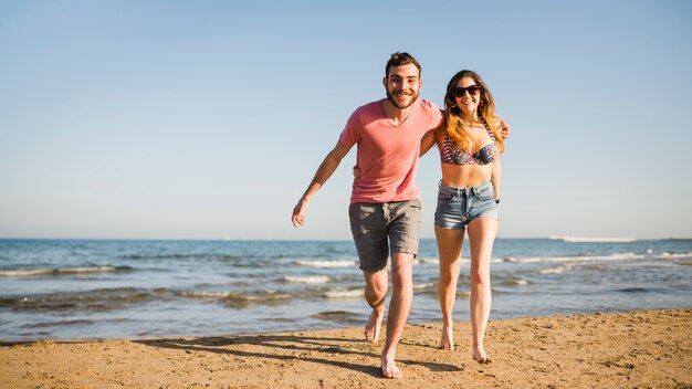 Lächelnde junge Paare, die zusammen auf Strand laufen