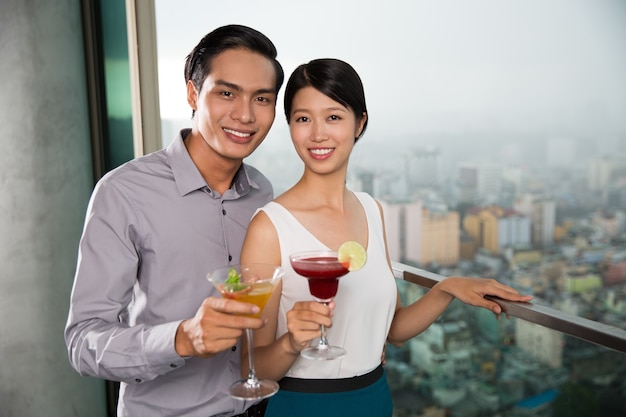 Lächelnde junge Paare mit Cocktails auf Balkon