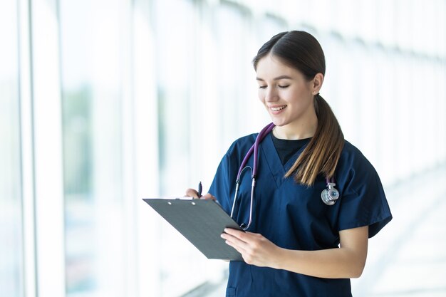 Lächelnde junge Ärztin, die eine Zwischenablage im Krankenhaus hält