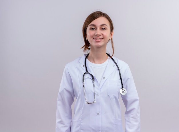 Lächelnde junge Ärztin, die medizinische Robe und Stethoskop auf isolierter weißer Wand mit Kopienraum trägt