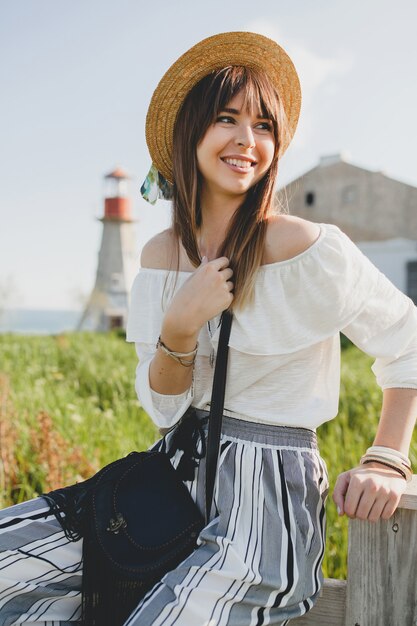 Lächelnde junge schöne stilvolle Frau, Frühling Sommer Modetrend, Boho-Stil, Strohhut, Landschaftswochenende, sonnige, schwarze Geldbörse