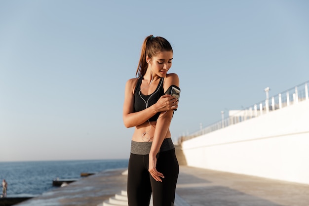 Lächelnde junge Sportfrau, die Musik mit Handy hört.