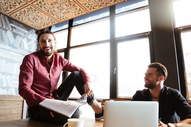 Lächelnde Kollegen, die im Büro sitzen und mit Dokumenten arbeiten.