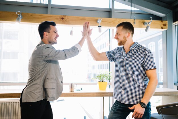 Lächelnde Männer, die Höhe-fünf im Büro geben