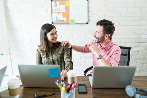 Lächelnde männliche und weibliche Geschäftsleute kommunizieren bei der Verwendung von Laptops am Schreibtisch