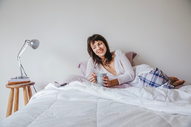 Lächelnde moderne Frau im Bett mit Kaffee