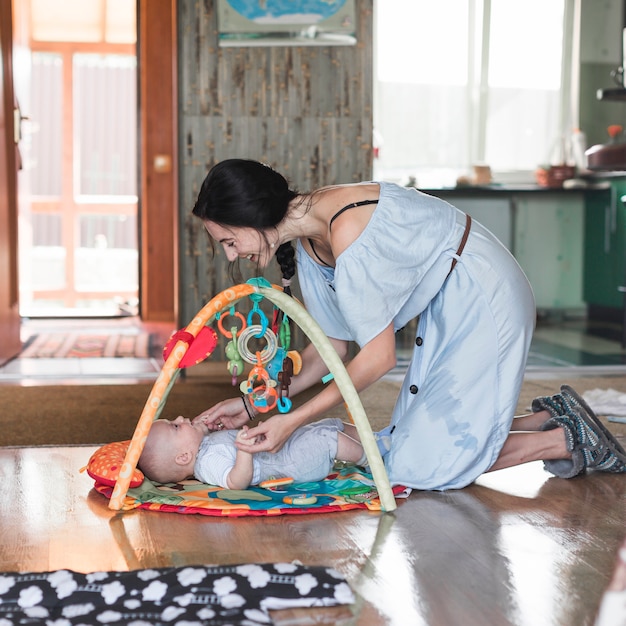 Lächelnde Mutter, die mit ihrem Baby liegt auf sich entwickelnder Wolldecke mit beweglichen pädagogischen Spielwaren spielt