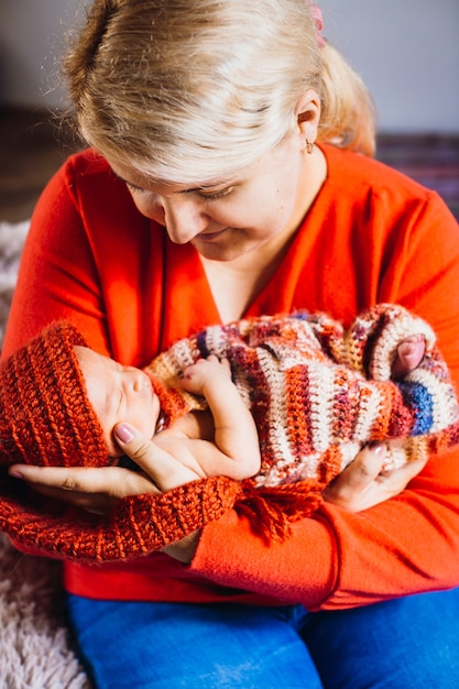 Lächelnde Mutter hält neugeborenes Baby im roten Hut auf ihren Armen an