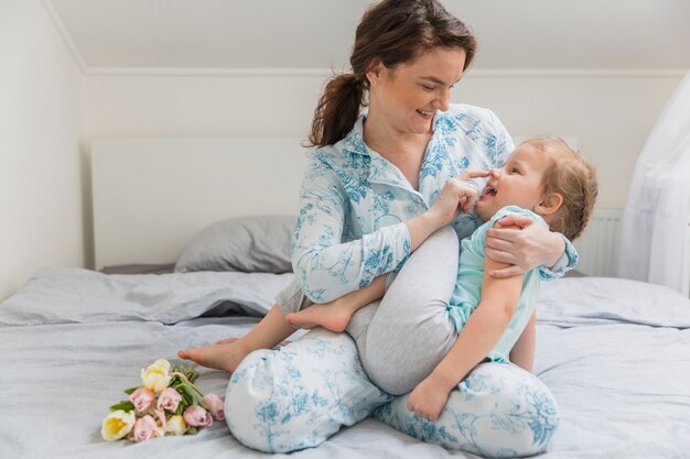 Lächelnde Mutter und Tochter, die auf Bett spielen