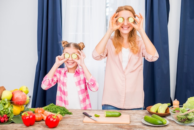 Lächelnde Mutter und Tochter, die Scheibe der Gurke vor ihren Augen halten