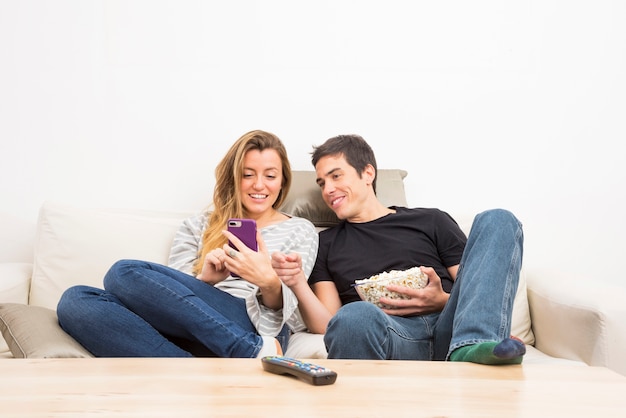 Lächelnde Paare, die den Handy sitzt auf dem Sofa betrachten