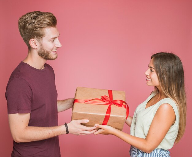 Lächelnde Paare, die Geschenkbox gegen farbigen Hintergrund halten