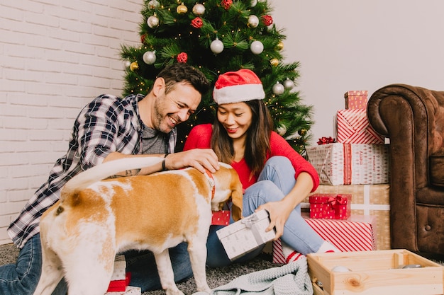 Lächelnde Paare, die Weihnachten mit Hund feiern