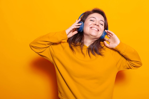 Lächelnde Person, die sich glücklich fühlt und Musik hört, mit modernen Kopfhörern vor der Kamera. Frau mit Lächeln, die ein Headset trägt, um Lieder und Audio zu hören, um Spaß und Unterhaltung zu haben.