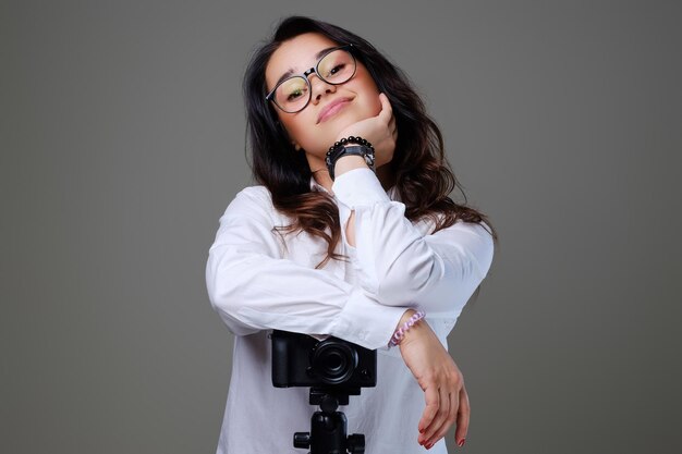 Lächelnde, positive brünette Frau mit Brille, die mit einer professionellen Fotokamera fotografiert. Isoliert auf grauem Hintergrund.