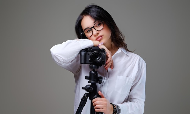 Lächelnde, positive brünette Frau mit Brille, die mit einer professionellen Fotokamera fotografiert. Isoliert auf grauem Hintergrund.