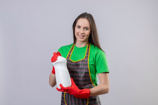 Lächelnde Reinigung des jungen Mädchens, das Uniform in den roten Handschuhen hält, die Reinigungsmittel auf lokalisiertem weißem Hintergrund halten