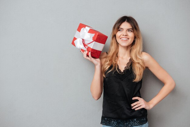 Lächelnde reizende Frau, die Geschenkbox hält und wegschaut