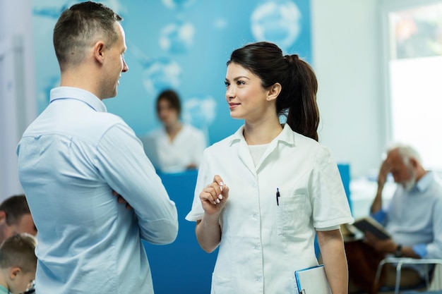 Lächelnde Ärztin, die mit männlichem Patienten kommuniziert, während sie in einem Flur in der Klinik steht