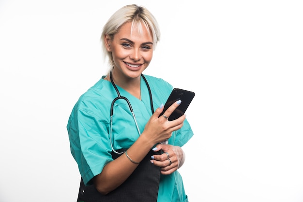 Lächelnde Ärztin, die Zwischenablage und Telefon auf weißer Oberfläche hält