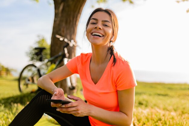 Lächelnde schöne Frau, die Telefon hält, das Sport am Morgen im Park tut