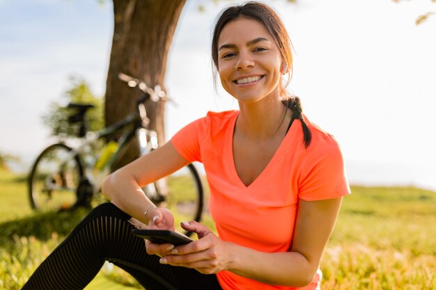 Lächelnde schöne Frau, die Telefon hält, das Sport am Morgen im Park tut