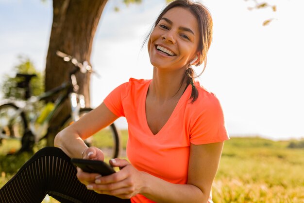 Lächelnde schöne Frau, die Telefon hält, das Sport am Morgen im Park tut