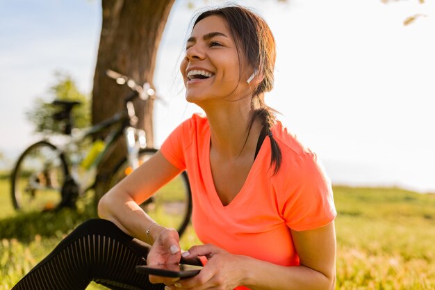 Lächelnde schöne Frau, die Telefon hält, das Sport am Morgen im Park tut