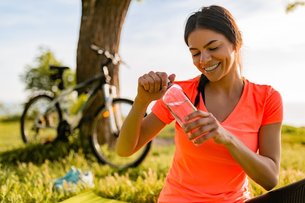 Lächelnde schöne Frau, die Wasser in der Flasche trinkt, die Sport am Morgen im Park tut