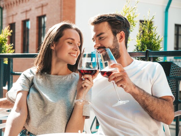 Lächelnde schöne Frau und ihr hübscher Freund Fröhliche fröhliche Familie Paar jubelt mit Gläsern Rotwein bei ihrem Date im Restaurant Sie trinken Alkohol im Veranda-Café auf der Straße