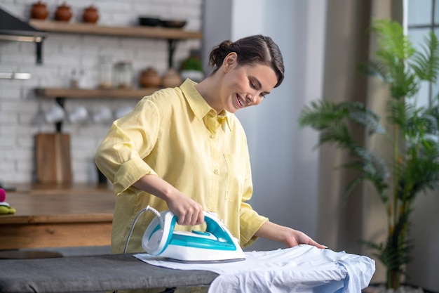 Lächelnde schöne Hausfrau, die das zerknitterte Hemd bügelt