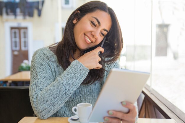 Lächelnde schöne junge Frau, die Smartphone und Tablette verwendet